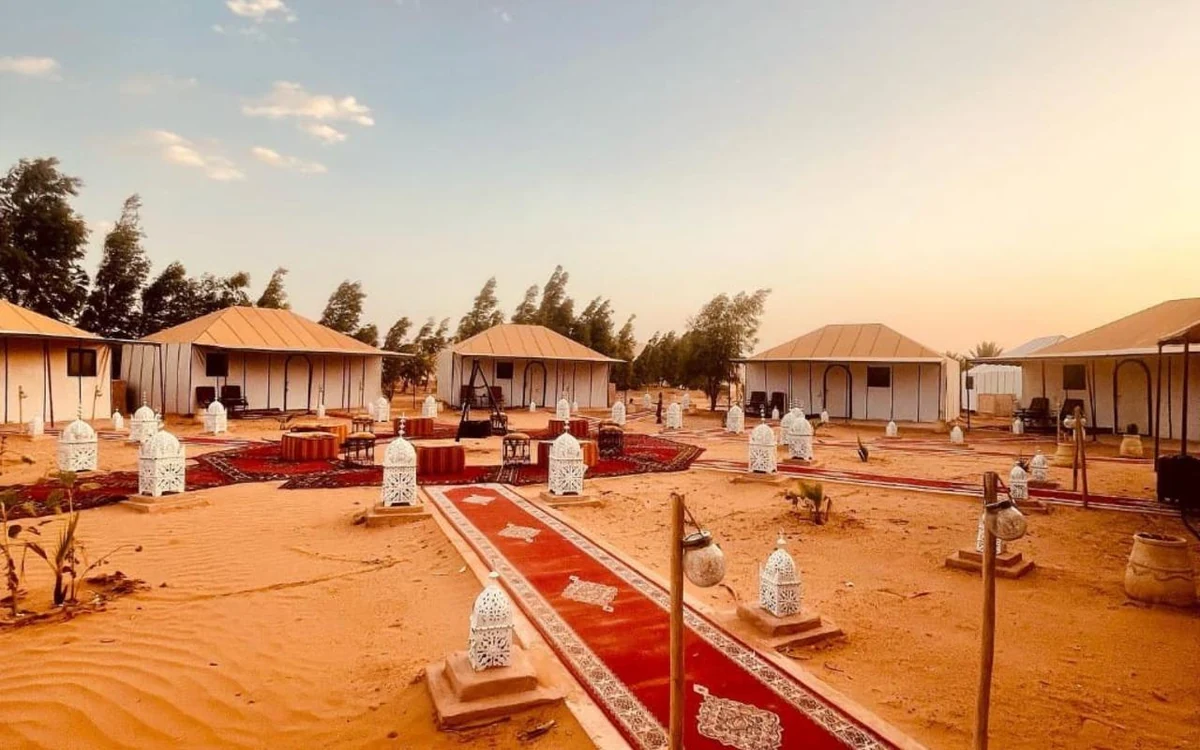 Rows of tents around carpets and lanterns at a desert camp at dusk