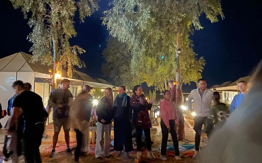 People standing outside a desert camp lit up after dark