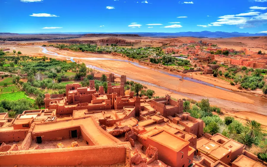 An earthen kasbah village above a green palm valley from above